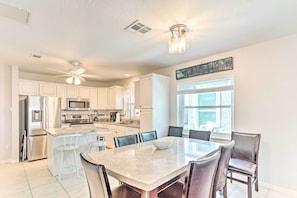 A modern kitchen with white cabinets, stainless steel appliances, and a central island with bar stools. - Oasis House at The Nettles Island Resort! (Jensen Beach)