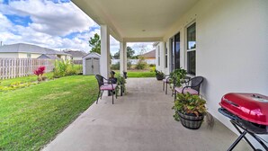 Eine überdachte Terrasse mit Gartenmöbeln, einem Grill und Kübelpflanzen.