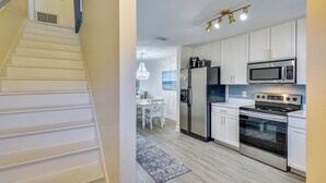 Una cocina moderna con armarios blancos, electrodomésticos de acero inoxidable y una zona de comedor con candelabro.