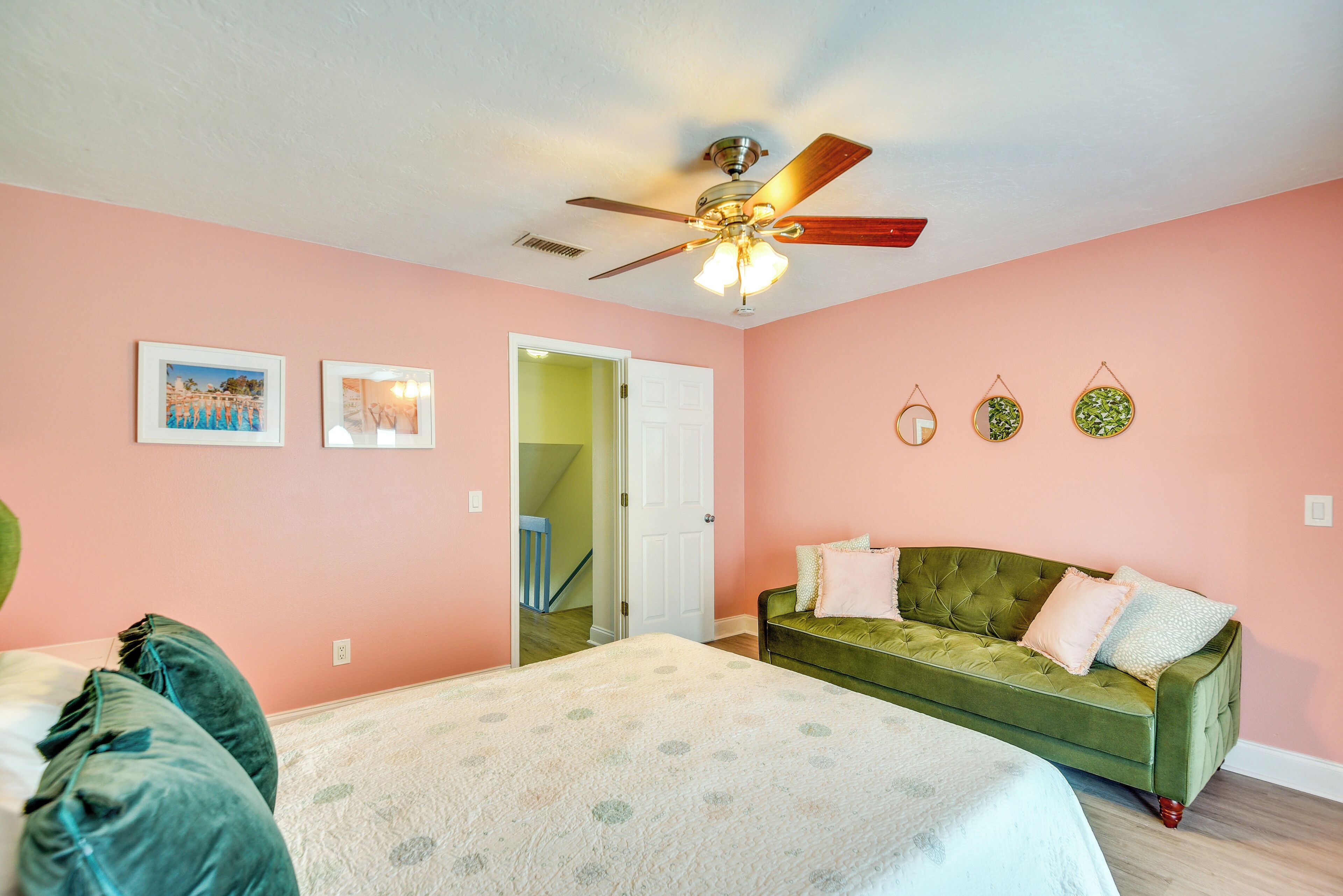 A bedroom with a bed, a green sofa, a ceiling fan, and a door leading to another room.