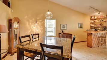 A dining area with a marble table and chairs, a wooden clock, and a kitchen area with a wooden bar and shelves.