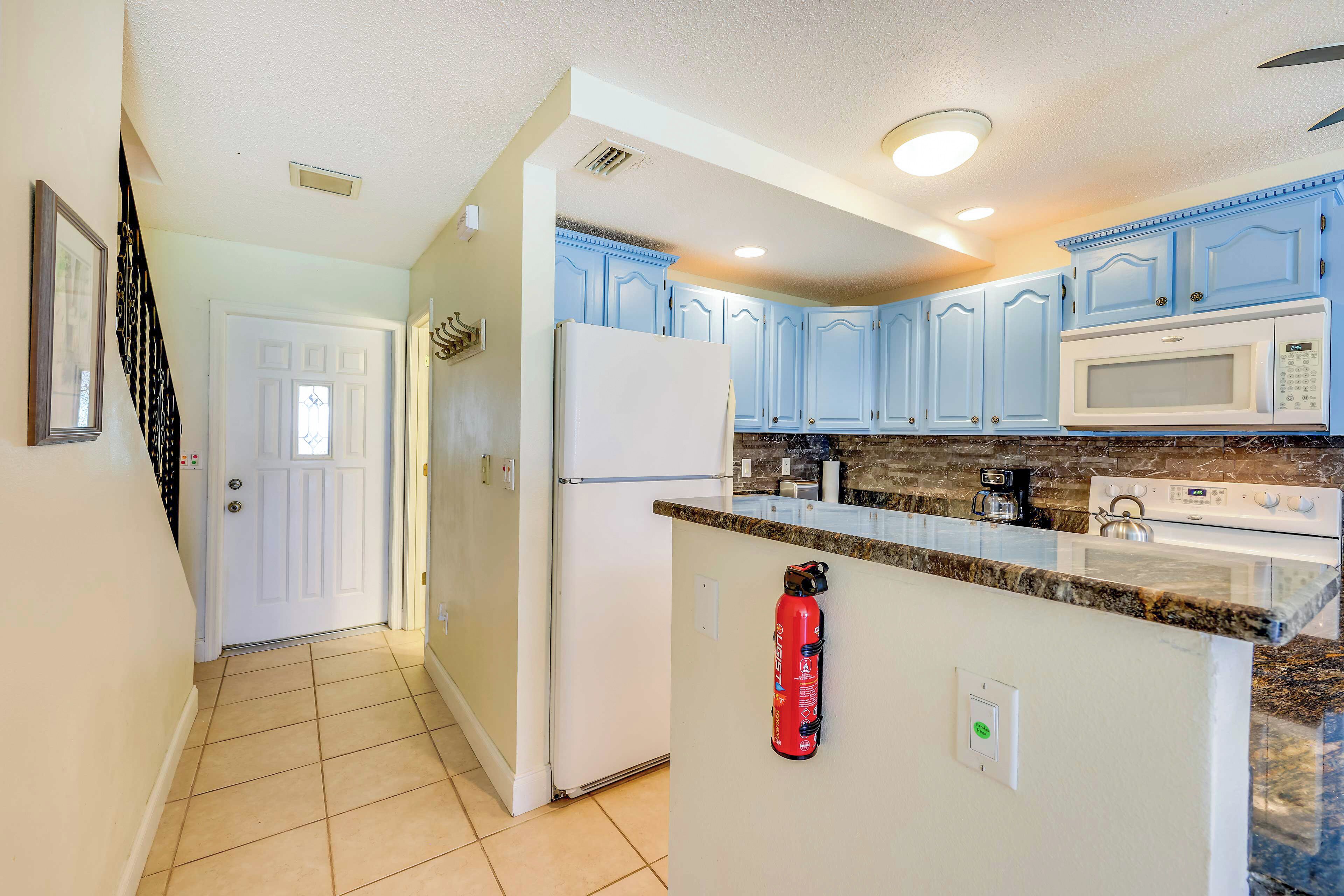 A kitchen with light blue cabinets, a white refrigerator, a microwave, and a stove.