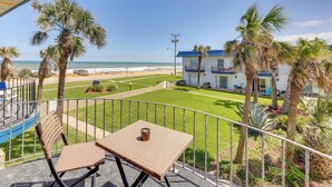 Ein Balkon mit Korbstühlen und einem Tisch, mit Blick auf einen Strand und eine gepflegte Rasenfläche mit Palmen.