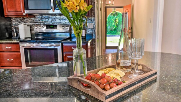 A kitchen counter with a wooden tray holding grapes, cheese, and a bottle of wine. There are two vases with flowers and two glasses on the counter. - Port Charlotte Retreat w/ Heated Pool & Spa! (Port Charlotte)