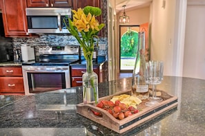A kitchen counter with a wooden tray holding grapes, cheese, and a bottle of wine. There are two vases with flowers and two wine glasses. - Port Charlotte Retreat w/ Heated Pool & Spa! (Port Charlotte)