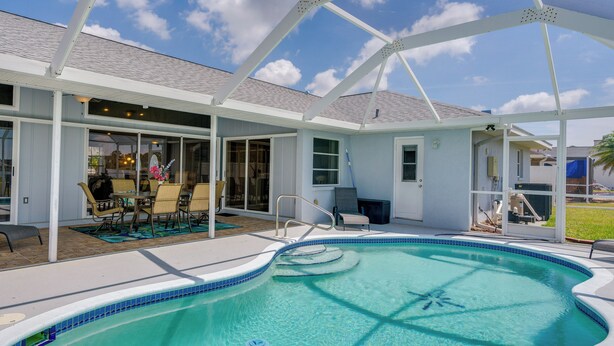 Une piscine couverte avec un espace patio, un coin salon abrité et une vue sur la maison en arrière-plan.