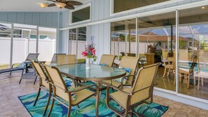 Une terrasse couverte avec une table ronde en verre, des chaises rembourrées et un vase décoratif.