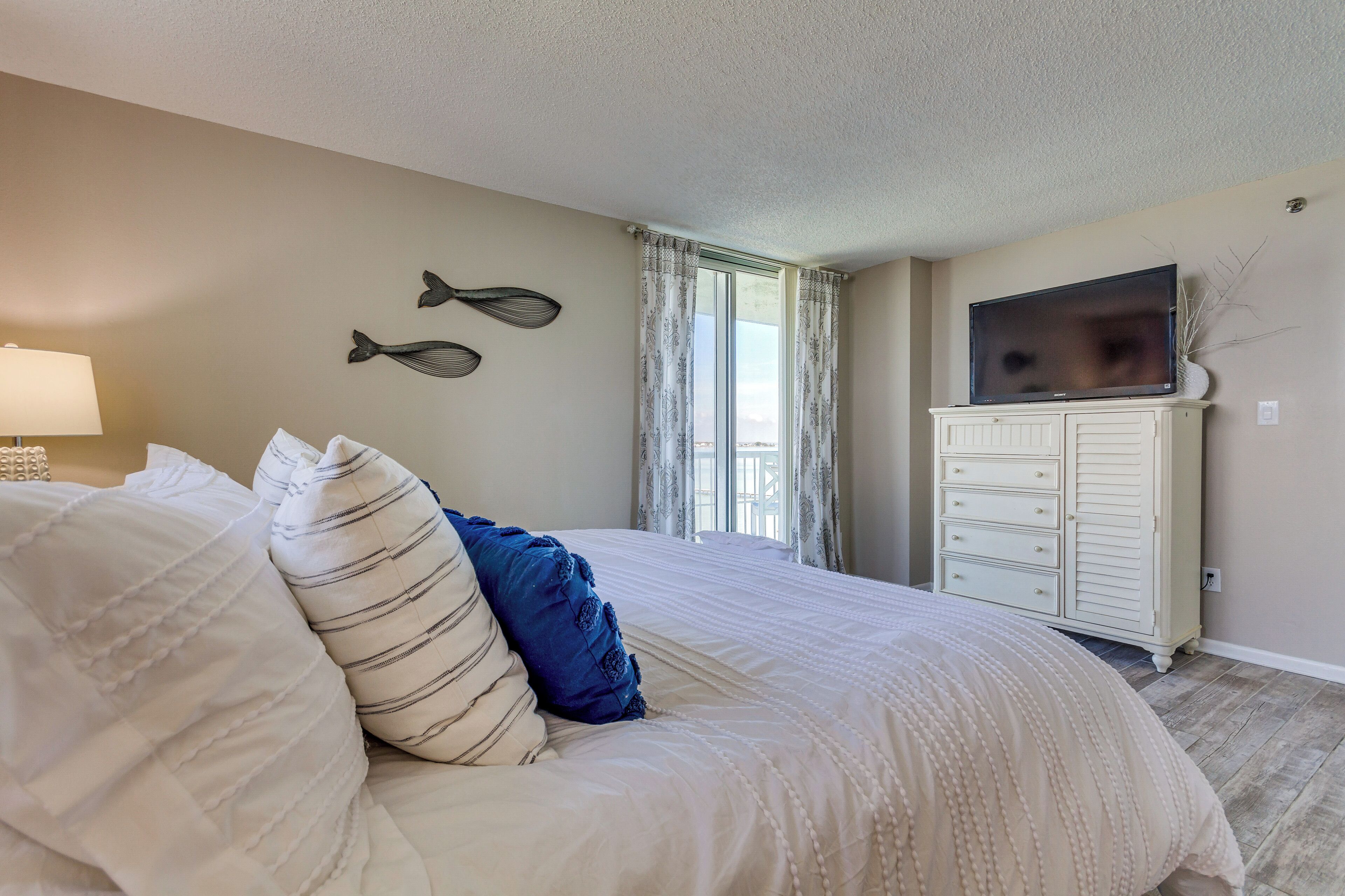 A bedroom with a large bed, a dresser, a television, and decorative fish wall art.