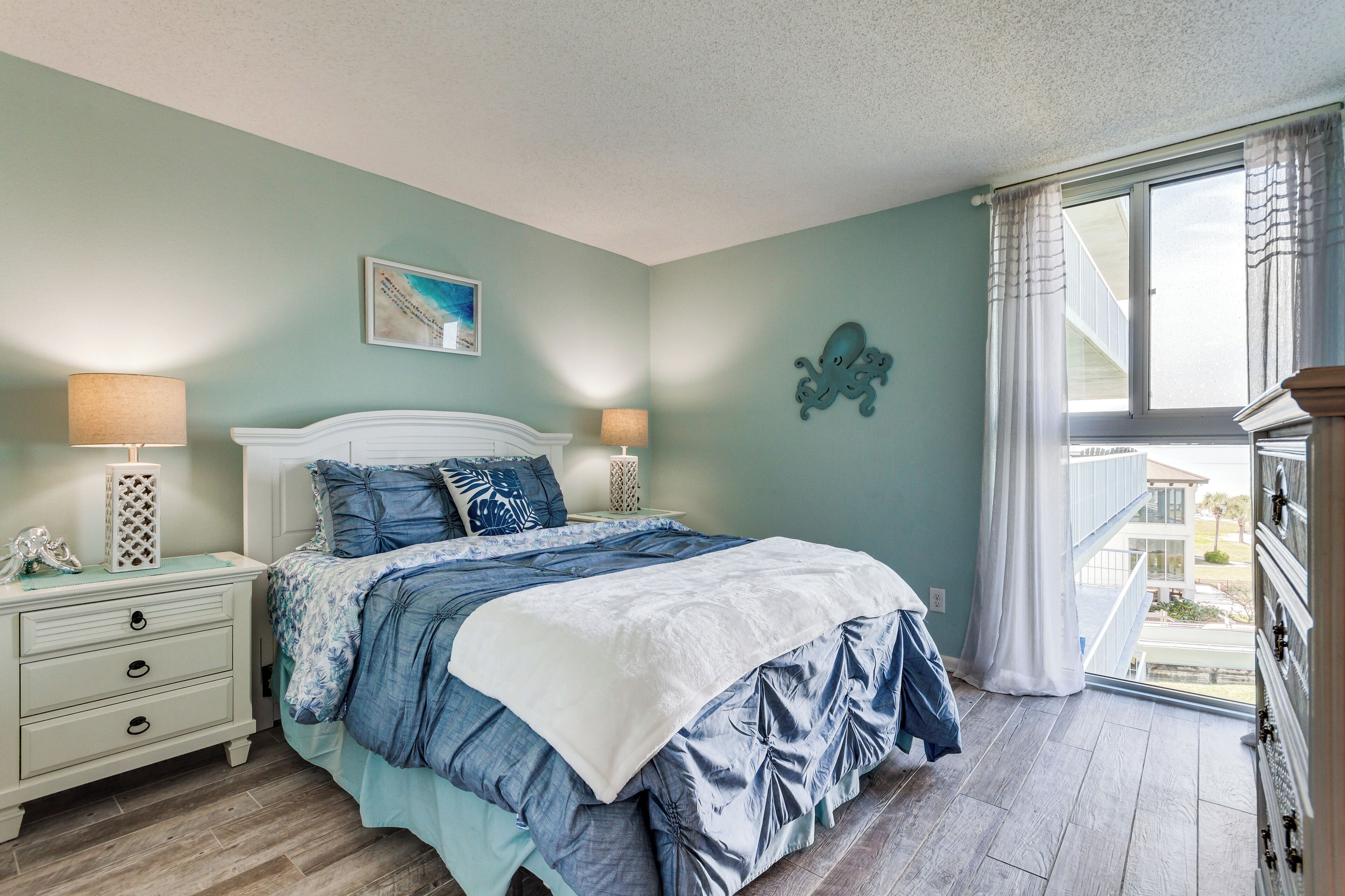 A bedroom with a bed, two bedside tables, a window with curtains, and a view of the outside.