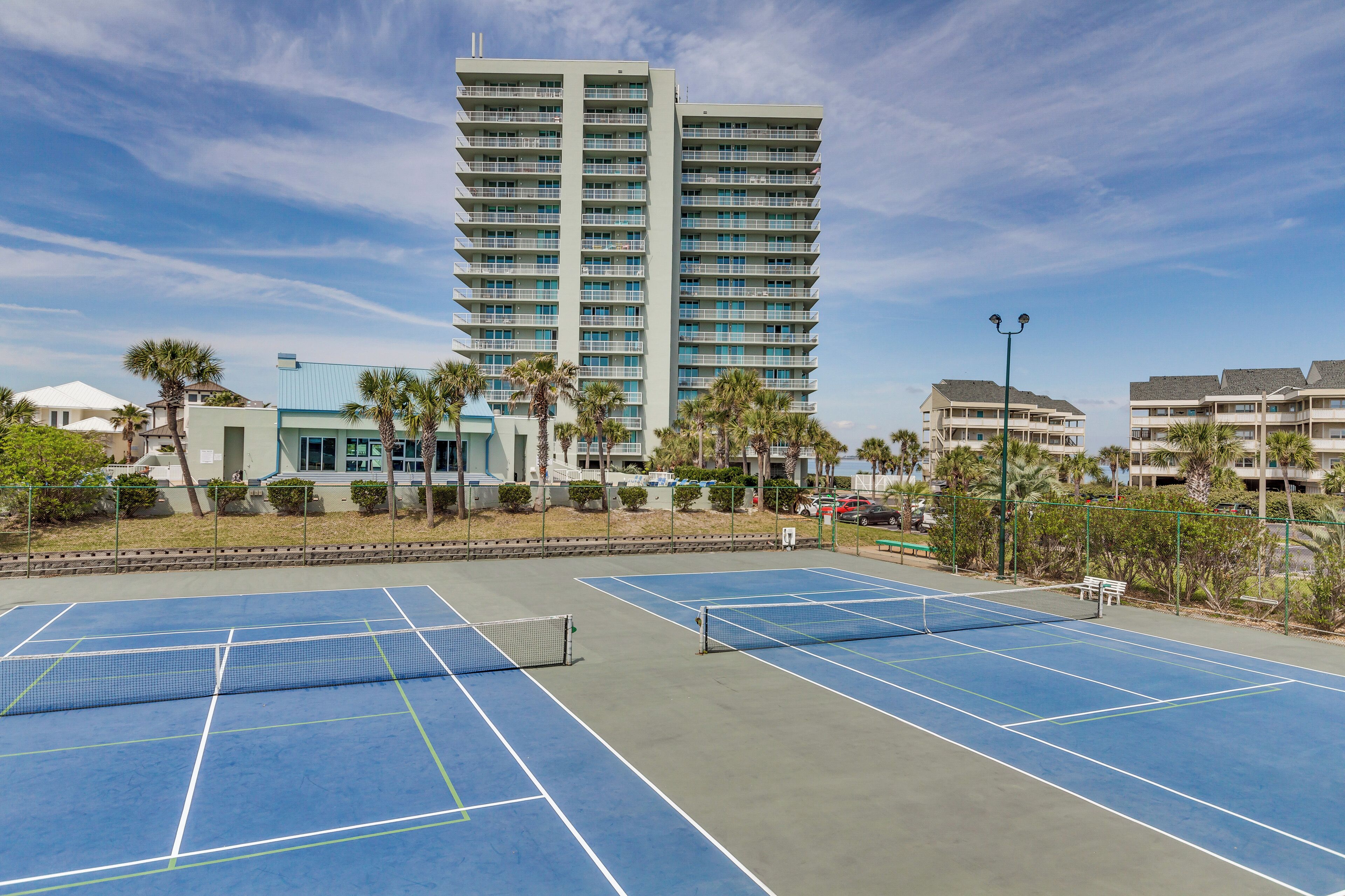 Una cancha de tenis con una red, rodeada de palmeras y edificios.
