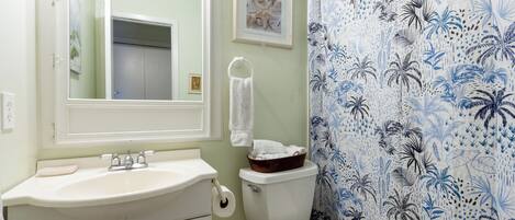 A bathroom with a white sink, toilet, and shower curtain with a tropical pattern.