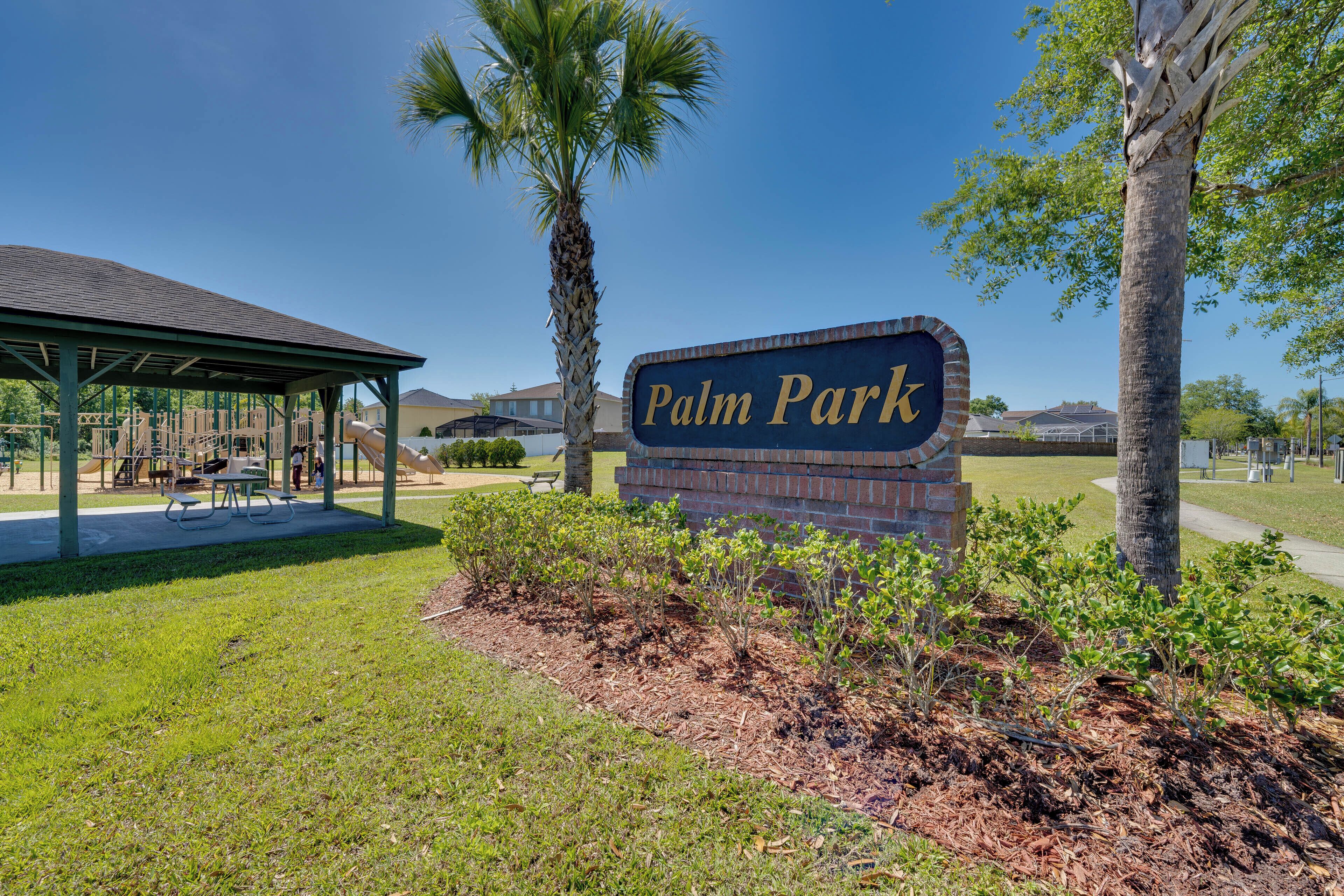 Un letrero de parque indica 'Palm Park', con un pabellón cubierto y juegos infantiles al fondo.
