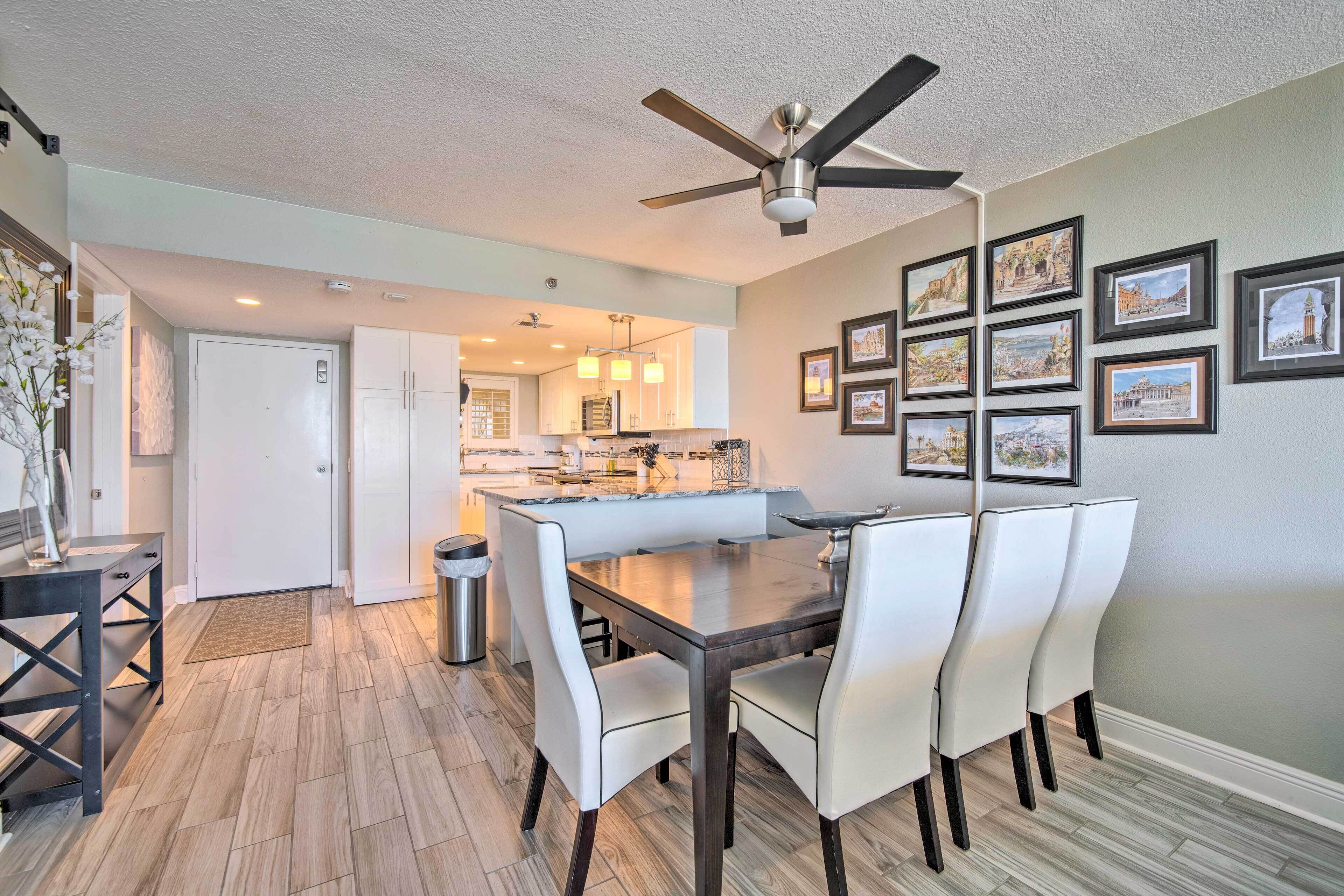 A dining area with a table and chairs, a ceiling fan, and framed pictures on the wall.