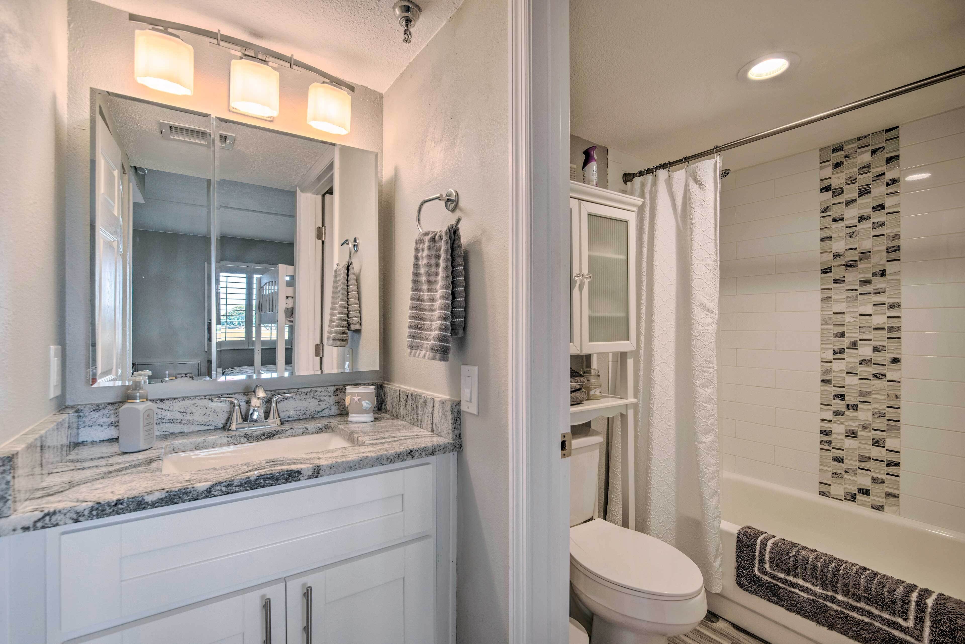 A bathroom with a marble sink, a large mirror, a toilet, and a shower with a patterned tile wall.