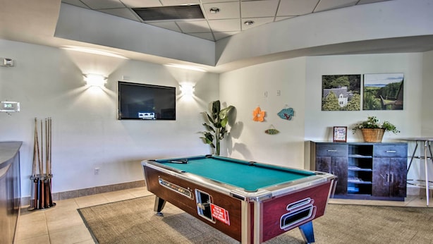 A pool table in a room with a flat-screen TV mounted on the wall, a potted plant, and a cabinet with shelves.