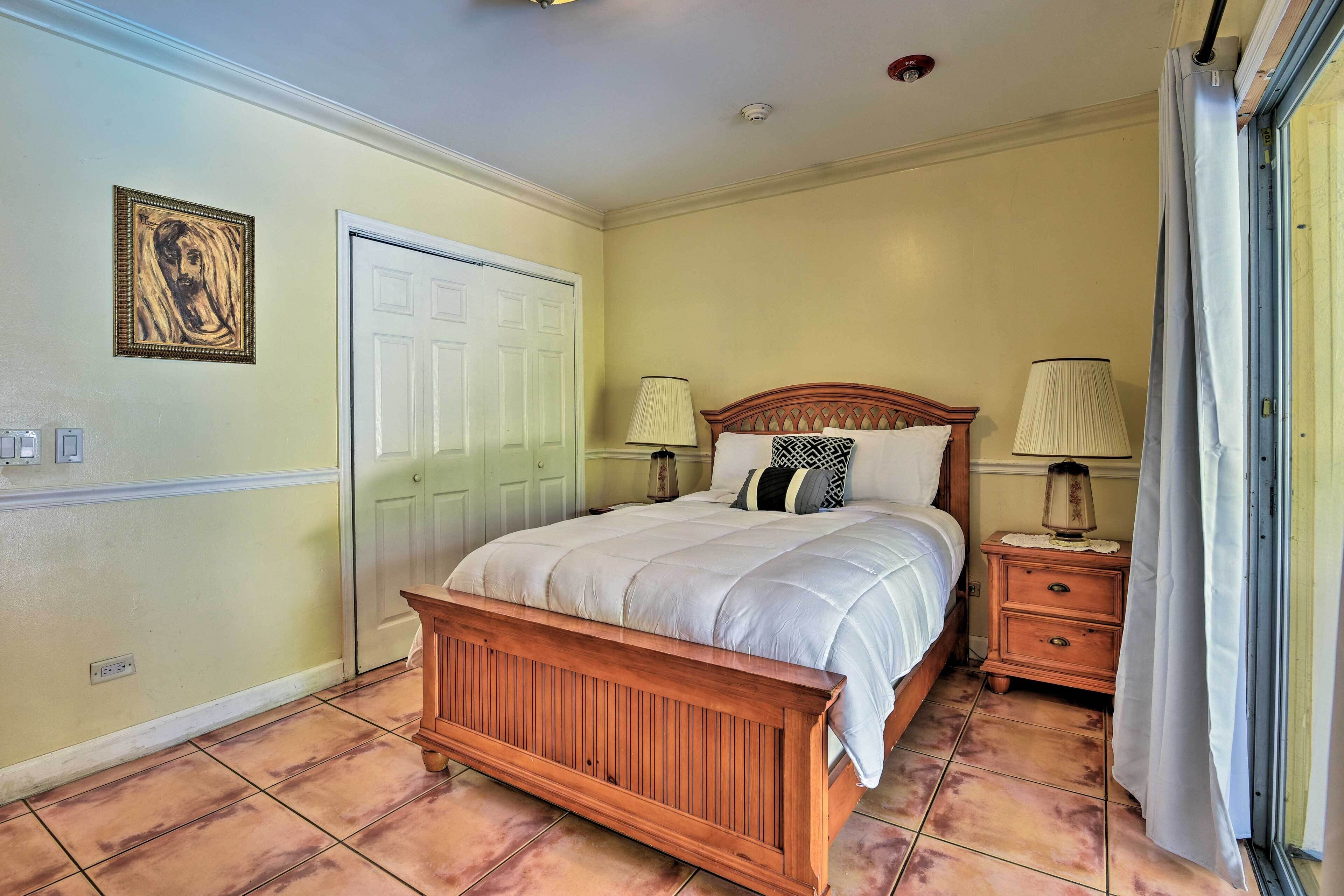 A bedroom with a wooden bed, two bedside tables with lamps, a door, and a wall-mounted picture.