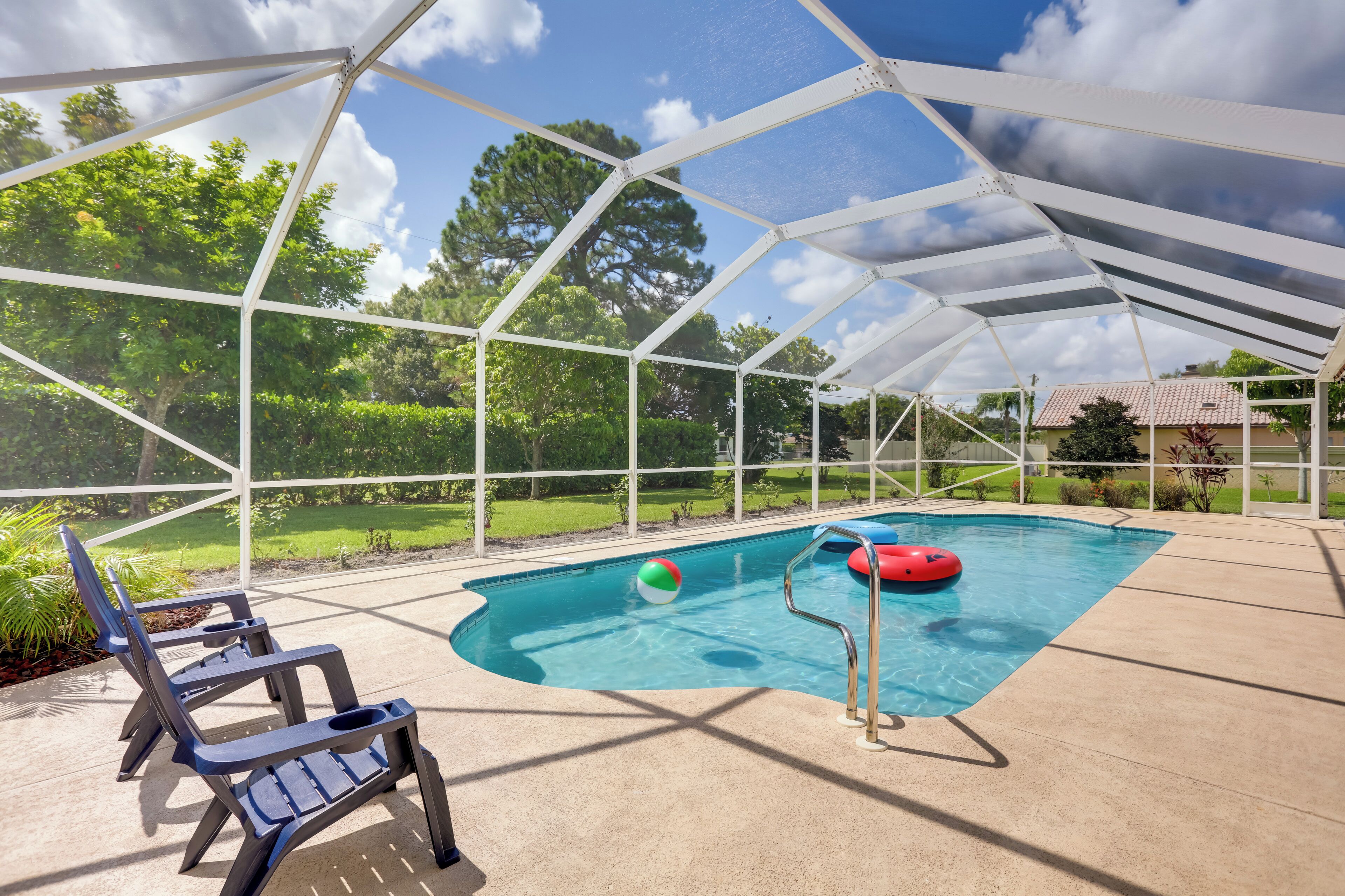 A covered outdoor swimming pool with a clear view of the surrounding greenery and a house in the background.