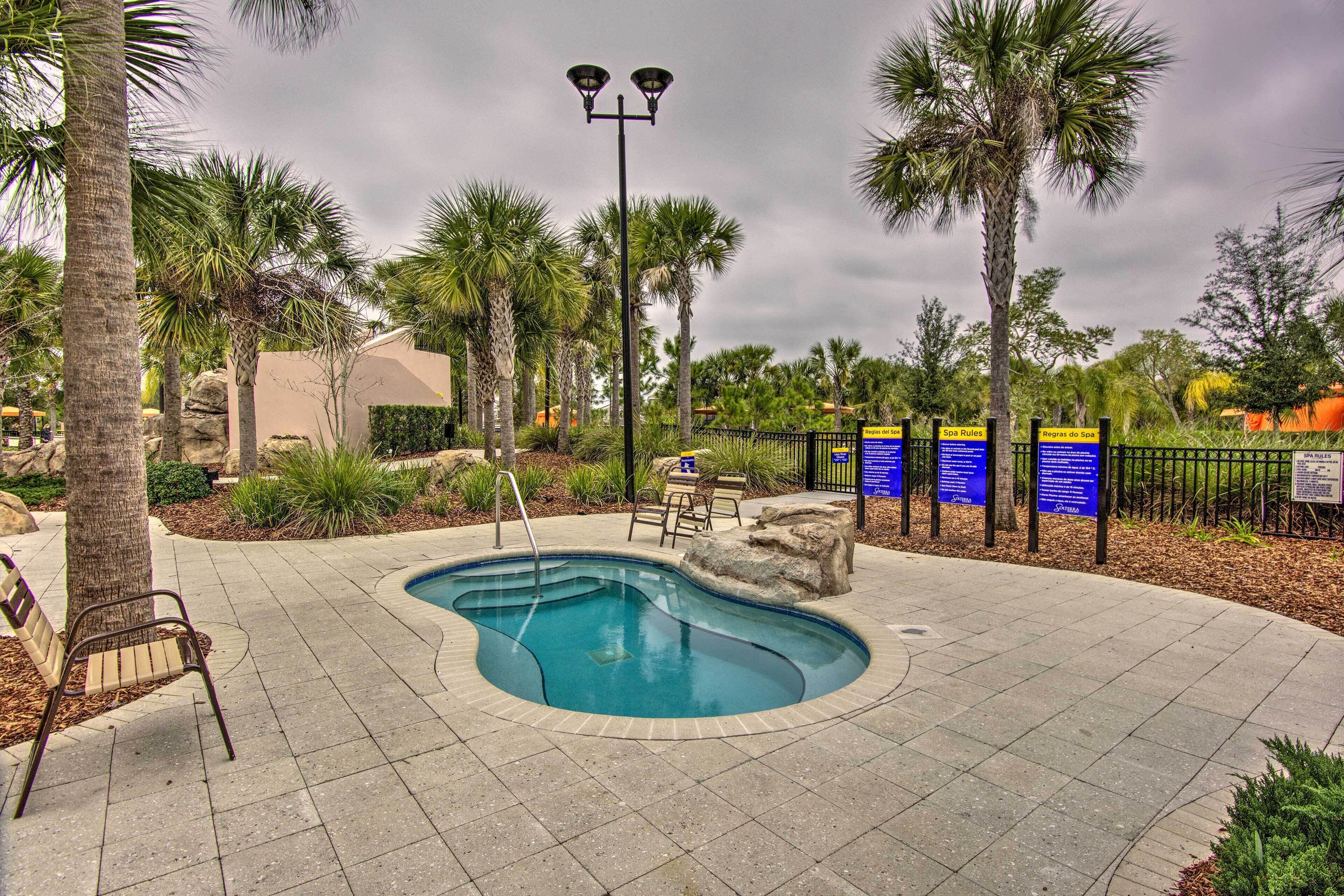 A swimming pool with a bench and a lamp post, surrounded by palm trees and a fence with informational signs.