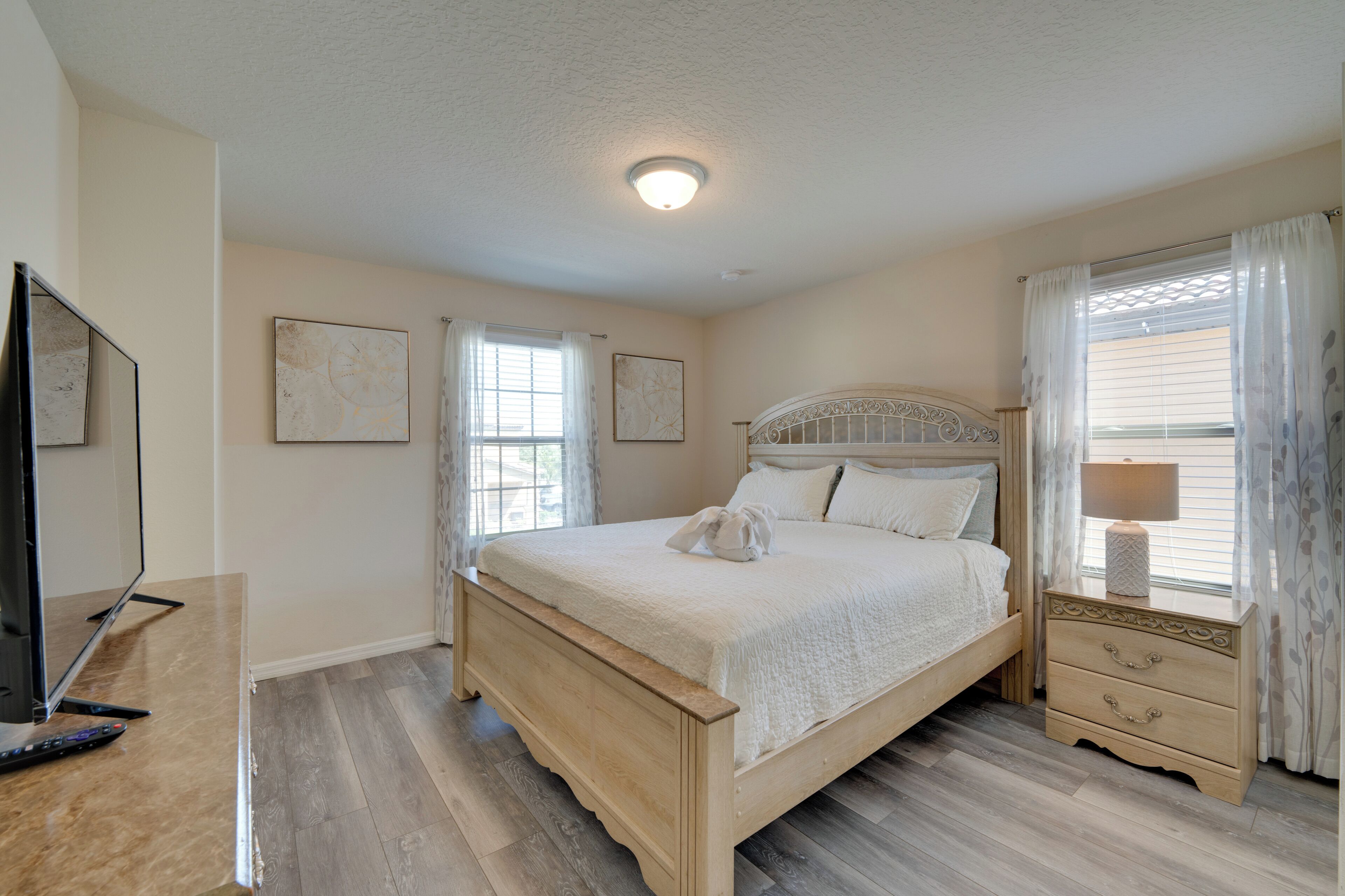 A bedroom with a wooden bed, a nightstand with a lamp, and a television on a stand.