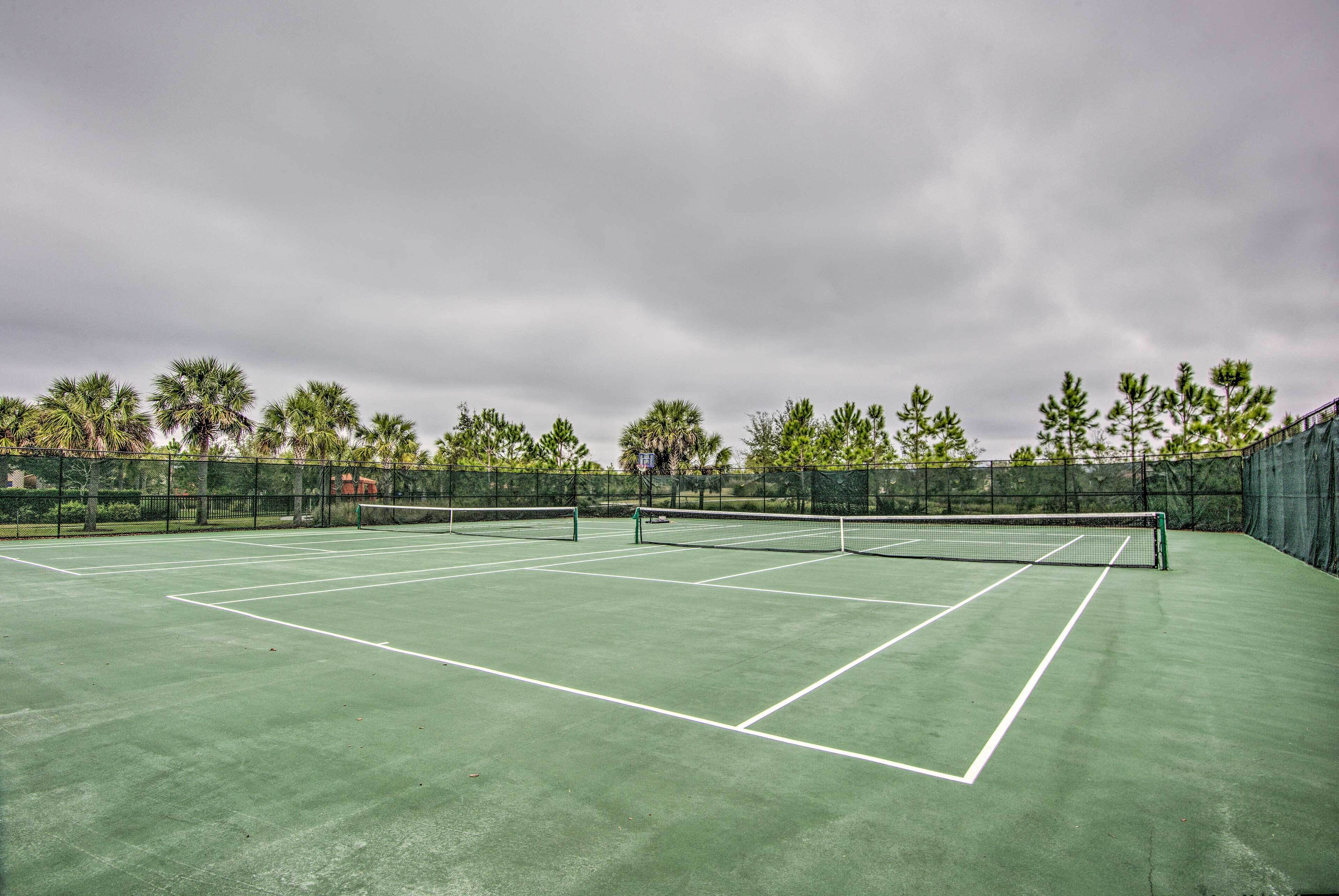 A tennis court with a net, surrounded by a fence and trees.