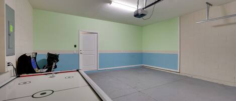 A room with a shuffleboard table, a door, and a light fixture on the ceiling.