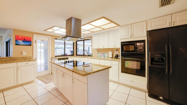 A modern kitchen with white cabinets, a granite countertop, a black refrigerator, and a built-in oven. - Relaxing Tampa Abode w/ Screened Lanai & Pool (Tampa)