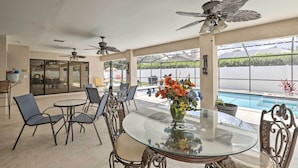 A covered outdoor dining area with a glass table, metal chairs, and ceiling fans. - Relaxing Tampa Abode w/ Screened Lanai & Pool (Tampa)