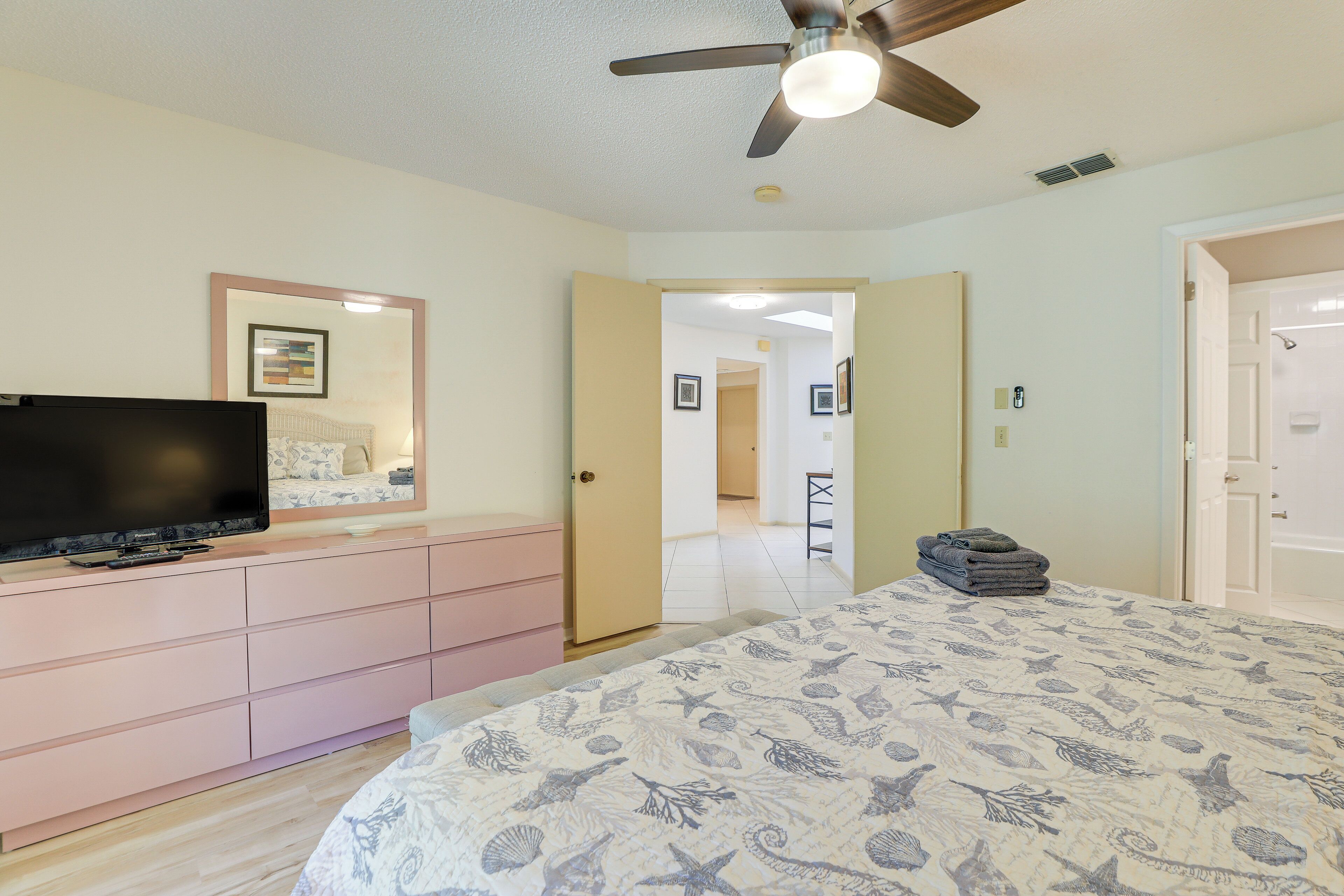 Quarto com cama, televisão em uma cômoda, ventilador de teto e porta para outro espaço.
