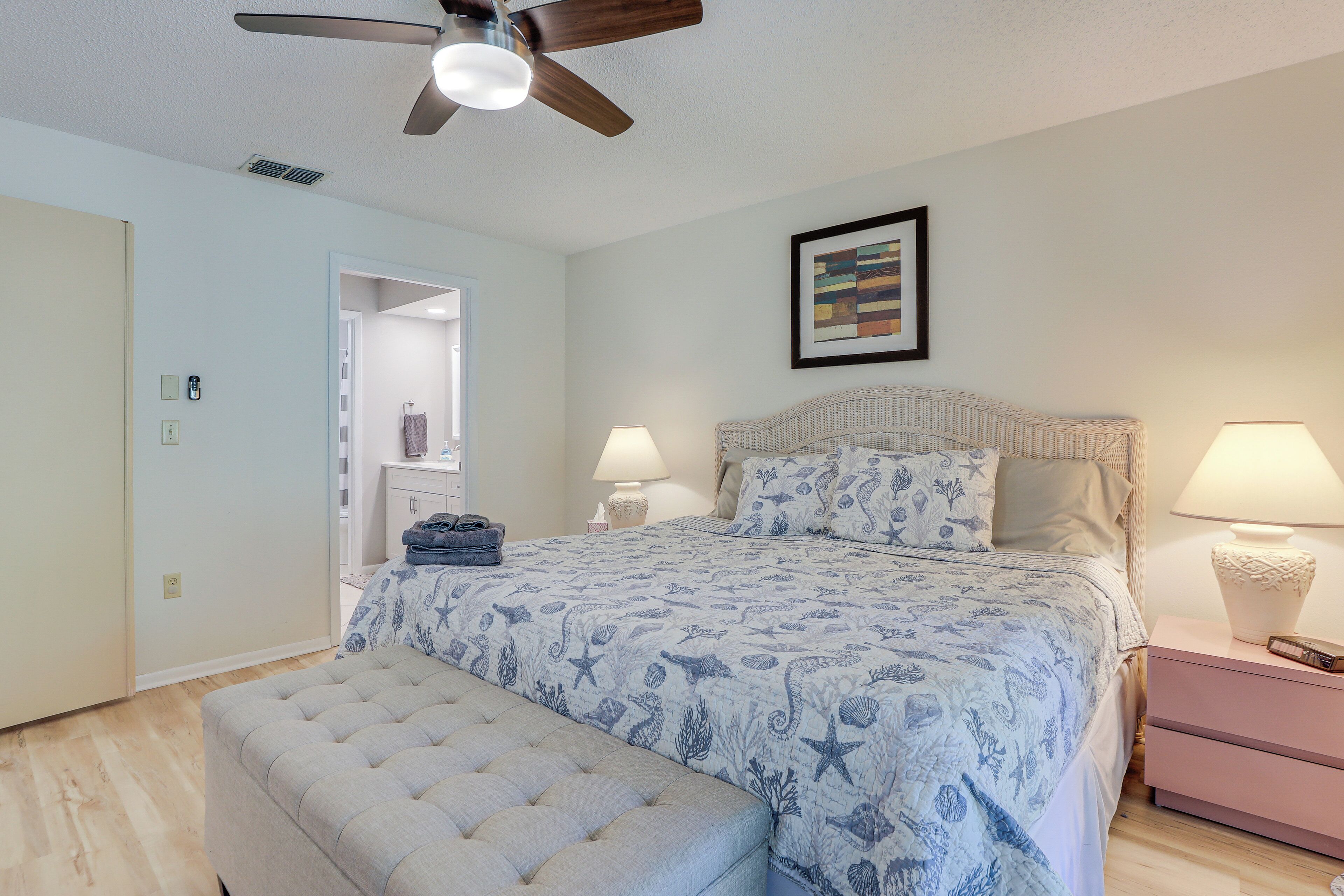 A bedroom with a bed, a bench, a ceiling fan, a nightstand, and a framed picture on the wall.
