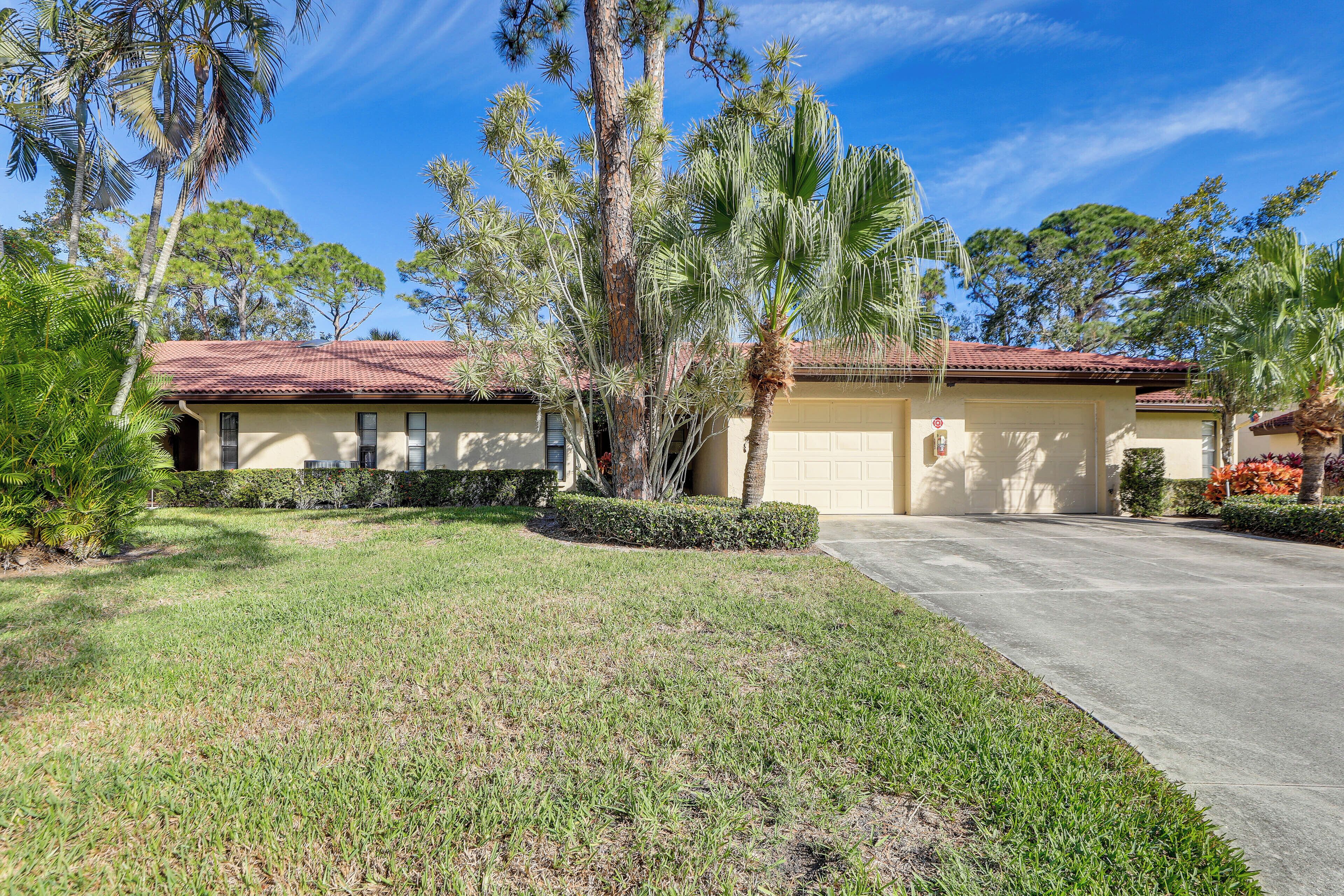 A residential house with a red-tiled roof, a well-maintained lawn, and several palm trees.