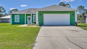 A single-story house with a green exterior, a white garage door, and a front yard with a sidewalk leading to the entrance. - Sebring Gem: Close to Golf & Raceway (Sebring)