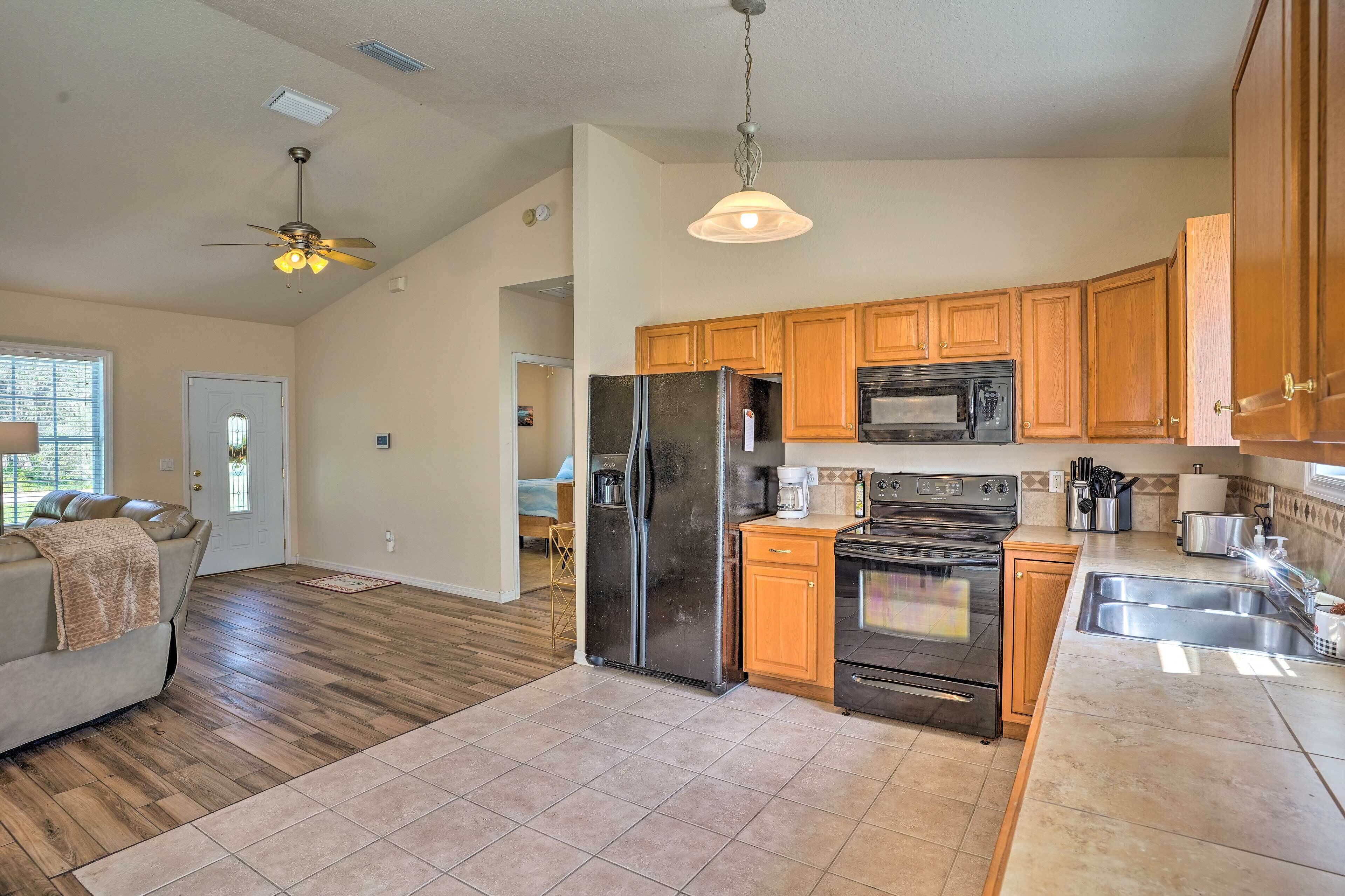 A modern kitchen with wooden cabinets, a refrigerator, stove, microwave, and a ceiling fan.