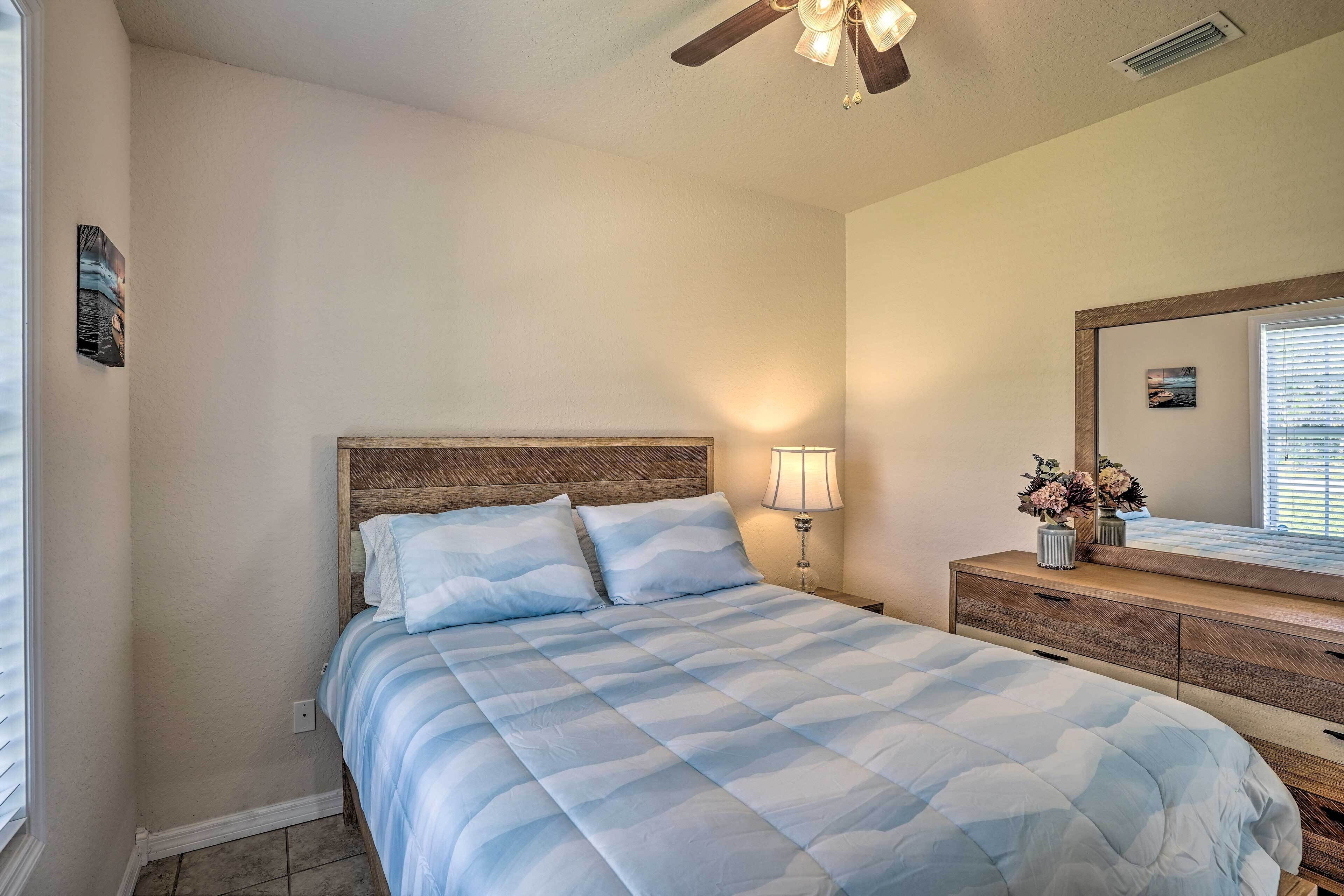 A bedroom with a bed, a nightstand, a dresser, a ceiling fan, and a window with blinds.