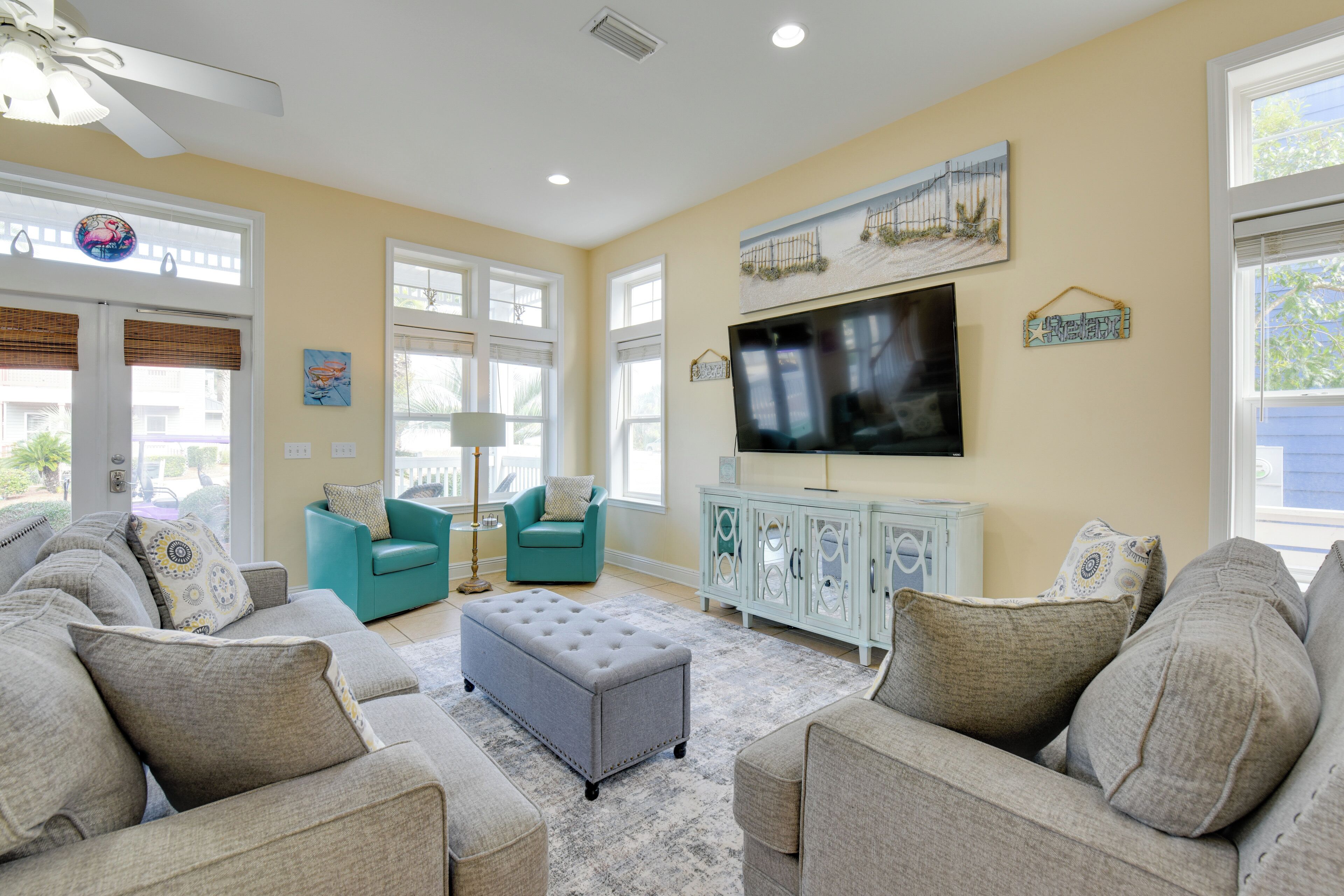 Un salon doté d’un grand téléviseur à écran plat, de fauteuils turquoise et d’un pouf gris.