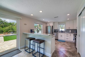 A modern kitchen with a large island, bar stools, and a view of a landscaped outdoor area. - Riverfront Home w/ Putting Green & Boat Dock! (New Port Richey)