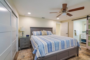 A bedroom with a bed, a nightstand, a lamp, a ceiling fan, and a bathroom with a mirror and towel rack. - Riverfront Home w/ Putting Green & Boat Dock! (New Port Richey)