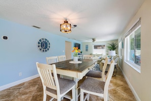 A dining area with a wooden table, white chairs, and a wall clock. - Riverfront Home w/ Putting Green & Boat Dock! (New Port Richey)