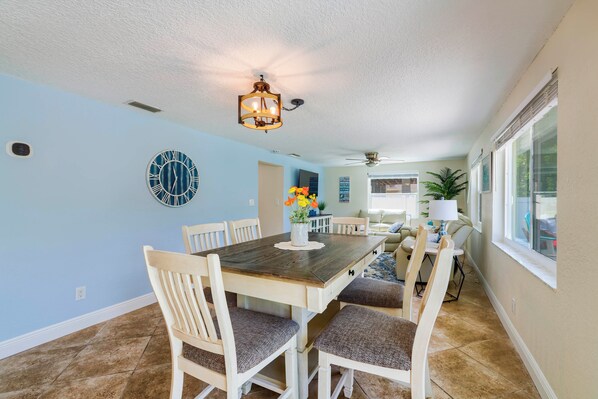 A dining area with a wooden table, white chairs, and a wall clock. - Riverfront Home w/ Putting Green & Boat Dock! (New Port Richey)