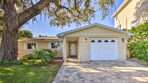 Une maison de plain-pied avec un garage, une allée pavée en briques et un grand arbre dont les branches sont recouvertes de mousse.