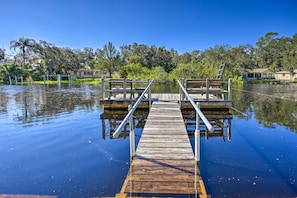 A wooden dock extending into calm water, surrounded by lush greenery and houses in the background. - Riverfront Home w/ Putting Green & Boat Dock! (New Port Richey)