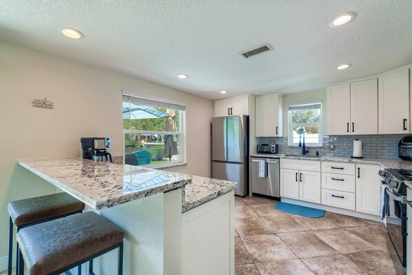 A modern kitchen with white cabinets, a stainless steel refrigerator, and a granite countertop. - Riverfront Home w/ Putting Green & Boat Dock! (New Port Richey)