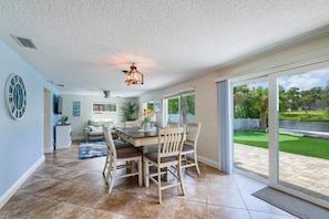 A spacious dining area with a wooden table and chairs, a ceiling fan, and a view of a green lawn through large sliding glass doors.