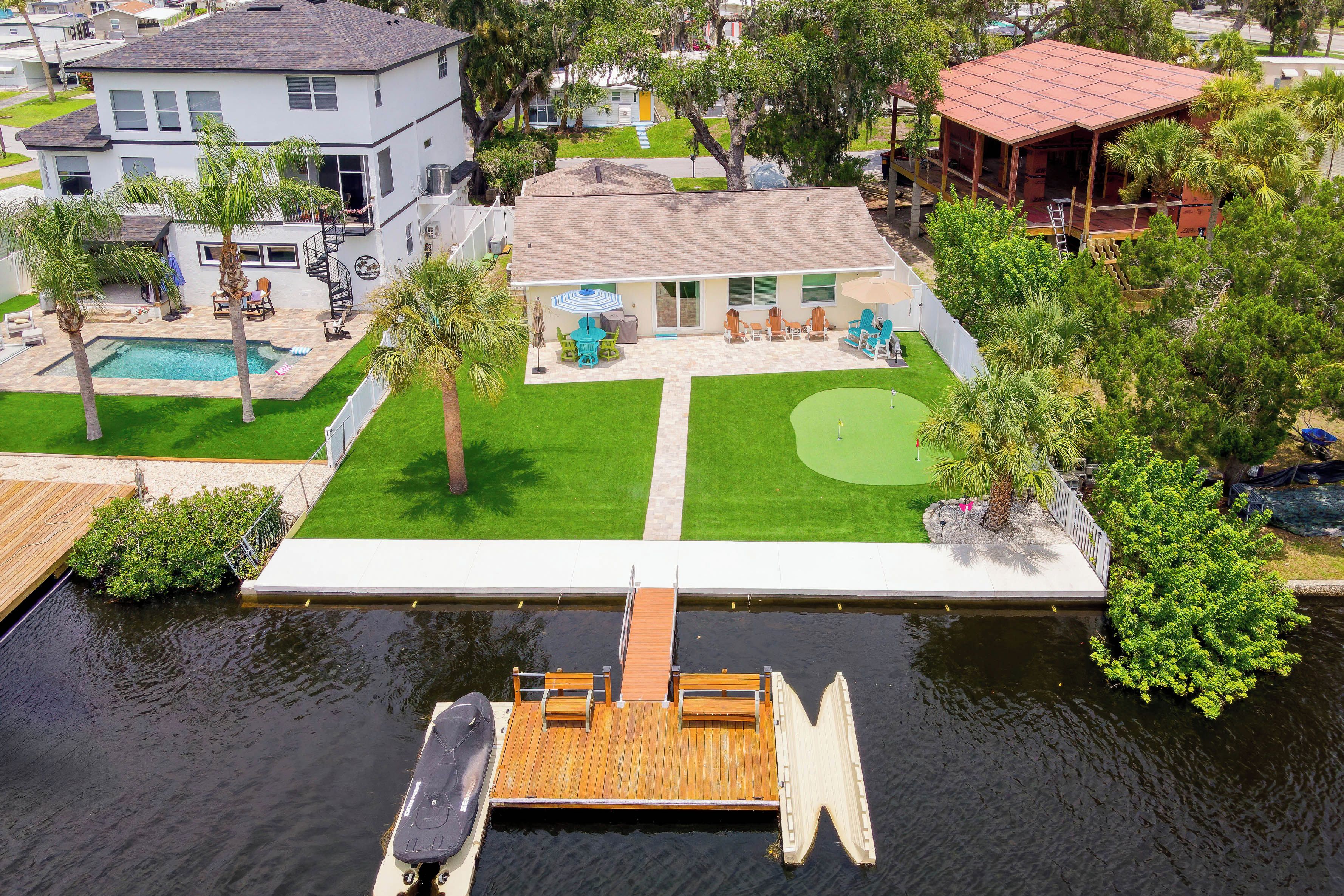A residential property with a swimming pool, a tennis court, and a dock extending into a body of water.