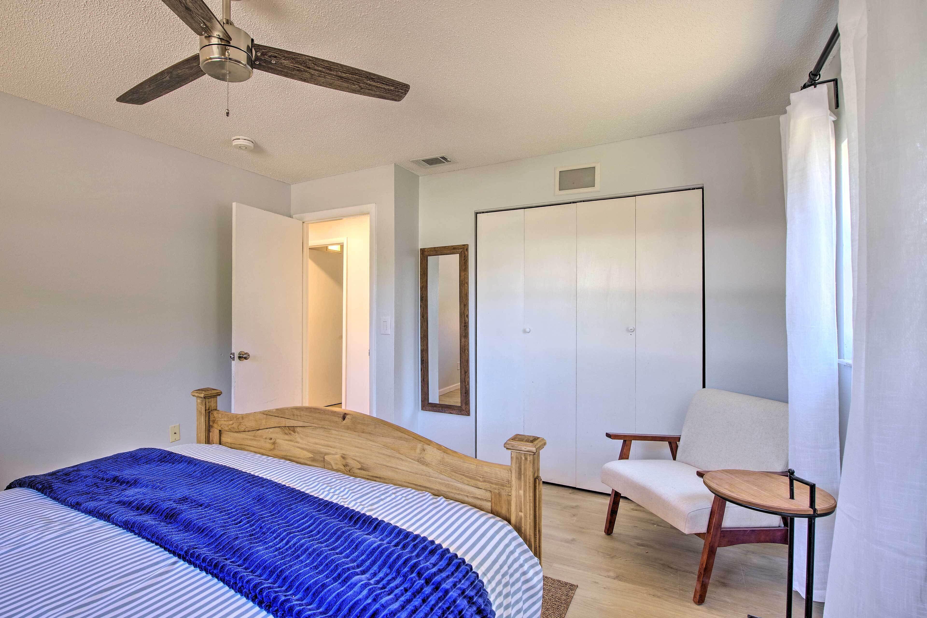 A bedroom with a bed, a wooden headboard, a ceiling fan, a chair, and a wardrobe.