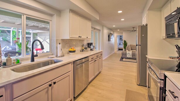 A modern kitchen with stainless steel appliances, white cabinetry, and a large window providing natural light.