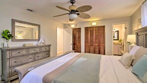 A bedroom with a bed, dresser, mirror, ceiling fan, and wooden closets.