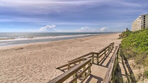 A beach with a wooden boardwalk leading to a building with multiple balconies.