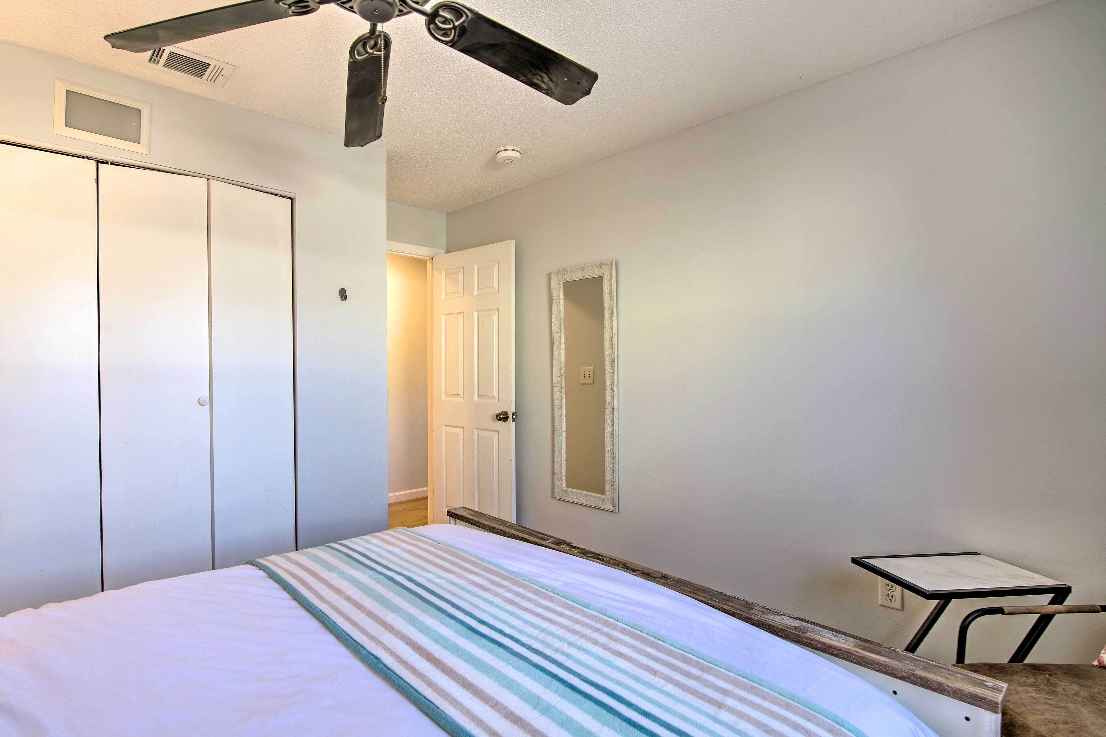 A bedroom with a bed, a ceiling fan, a wardrobe, a door, a mirror, and a small table.