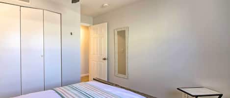 Une chambre à coucher comprenant un lit, un ventilateur de plafond, une armoire, une porte, un miroir et une petite table.