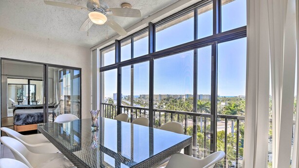 A modern dining area with a glass table and white chairs, large windows offering a city view.